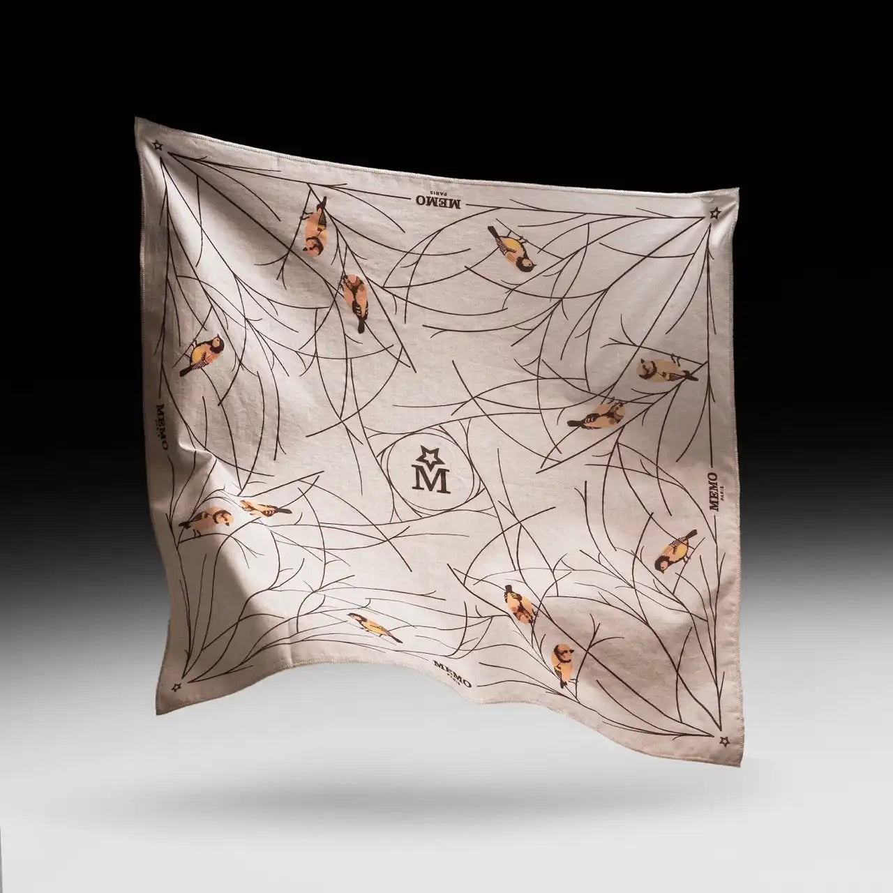 A light-colored square scarf featuring a pattern of bare tree branches and small, colorful birds, with a central ’M’ logo.