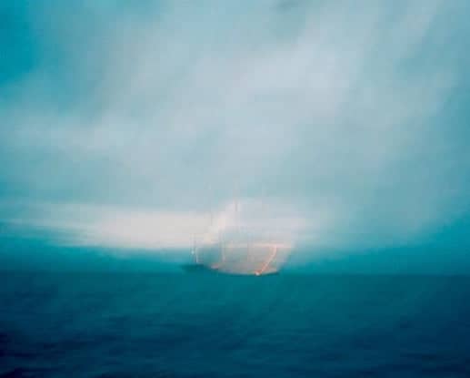 A glowing, translucent orange and white object floats on the dark blue ocean under a hazy sky.