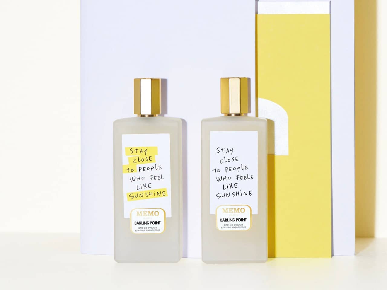 Two identical transparent glass perfume bottles with gold caps and handwritten-style labels reading ’stay close to people who feel like sunshine’ by darling point.