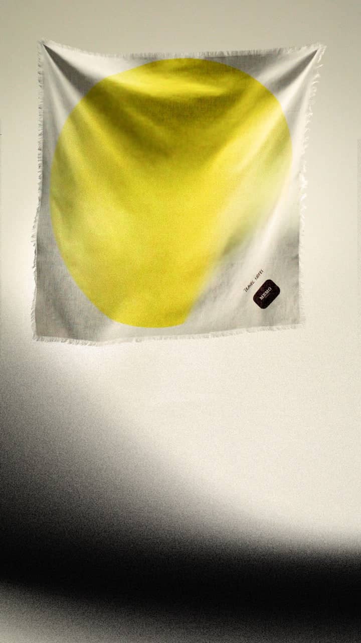 A vibrant yellow circular design on a white silk scarf with frayed edges.