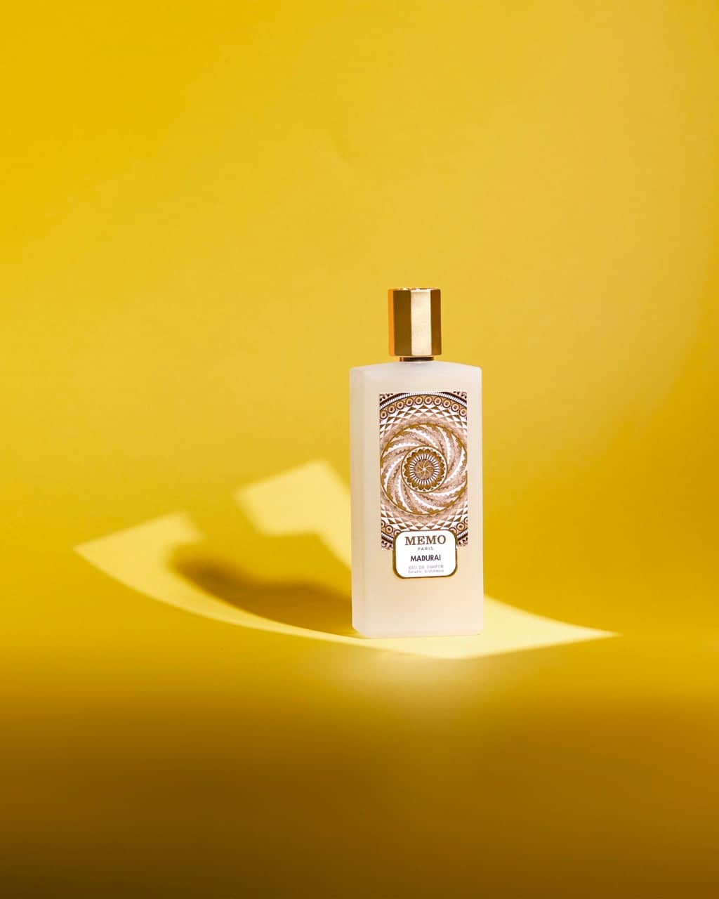 A white rectangular bottle of memo mankai perfume with a gold cap and an ornate label featuring intricate spiral patterns.